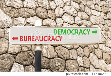 Democracy or bureaucracy words symbol. Concept words Democracy Bureaucracy on beautiful white road sign. Beautiful stone wall background. Business democracy bureaucracy concept. Copy space Democracy or bureaucracy words symbol. Concept words Democracy Bureaucracy on beautiful white road sign. Beautiful stone wall background. Business democracy bureaucracy concept. Copy space 142486558