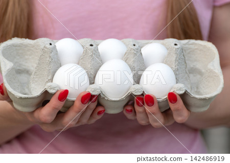 Woman's manicured hands in a pink shirt holding a gray egg carton of fresh white eggs, close up view suggesting healthy eating, cooking, baking and natural farm produce Woman's manicured hands in a pink shirt holding a gray egg carton of fresh white eggs, close up view suggesting healthy eating, cooking, baking and natural farm produce 142486919