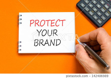 Protect your brand words symbol. Concept words Protect your brand on beautiful white note. Beautiful orange background. Businessman hand. Business and protect your brand concept. Copy space. Protect your brand words symbol. Concept words Protect your brand on beautiful white note. Beautiful orange background. Businessman hand. Business and protect your brand concept. Copy space. 142486989