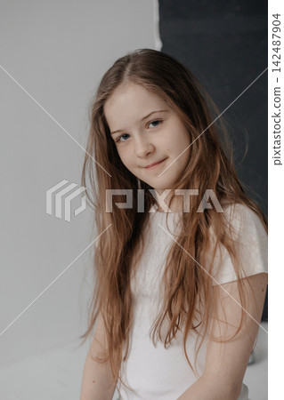 Dreamy preteen girl with long hair leaning against empty white wall copyspace Dreamy preteen girl with long hair leaning against empty white wall copyspace 142487904