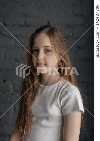 Cheerful preteen girl with long hair smiling against dark brick wall background Cheerful preteen girl with long hair smiling against dark brick wall background 142487906