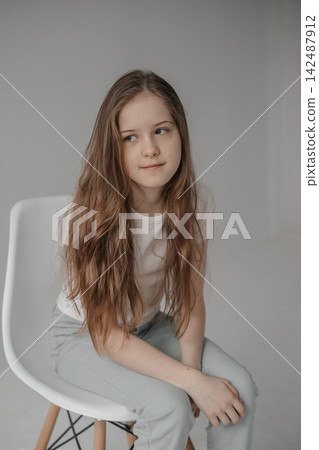 Preteen girl with long hair looking away while sitting on white chair in studio Preteen girl with long hair looking away while sitting on white chair in studio 142487912