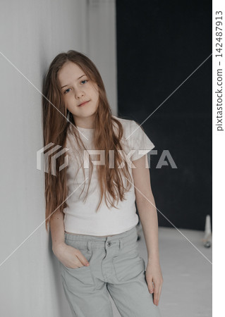 Dreamy preteen girl with long hair leaning against empty white wall copyspace Dreamy preteen girl with long hair leaning against empty white wall copyspace 142487913