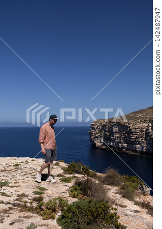 Traveler walking on a high rocky cliff edge with a scenic sea and bay view in Malta. Traveler walking on a high rocky cliff edge with a scenic sea and bay view in Malta. 142487947