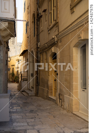 Narrow historic old town street with stone buildings and yellow doors in Mdina,Malta.  142487976