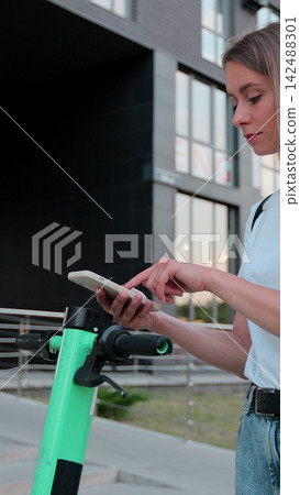 Vertical video. Woman scanning qr code on electric scooter, rental service app. Alternative transportation in city. Vertical video. Woman scanning qr code on electric scooter, rental service app. Alternative transportation in city. 142488301