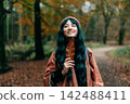 Young smiling woman in warm Shawl Poncho holding fallen leaf and enjoying the moment of calm and freedom in autumn forest walk. Feeling harmony, reunion with nature. Relaxing, mental recovery. 142488411