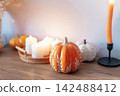 Cozy warm autumn home interior - decorative orange ceramic pumpkins, candles, dried flowers on the wooden console with white wall background. Scandinavian minimalist hygge home fall decor 142488412