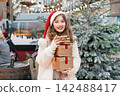 Young woman in Santa hat with with a tower of gift boxes on traditional city street Christmas market. Happy woman choosing Christmas gifts. Merry Xmas Happy New Year festive shopping, sales, discount. 142488417