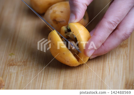 Slicing fresh fruit. Hand holding loquats. Yellow fruit hand. medlar in hand, close-up. High quality photo Slicing fresh fruit. Hand holding loquats. Yellow fruit hand. medlar in hand, close-up. High quality photo 142488569