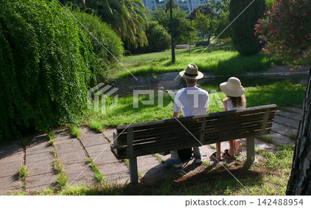 father and daughter are sitting on a bench in the park father and daughter are sitting on a bench in the park 142488954