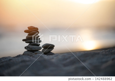 Stones stacked on beach during sunset with water in background Stones stacked on beach during sunset with water in background 142488962
