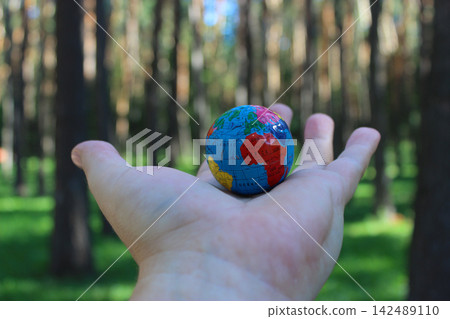 A model of the Earth lies on the open palm of a man in a park on a sunny day A model of the Earth lies on the open palm of a man in a park on a sunny day 142489110