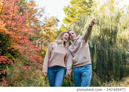 Young happy Caucasian couple in love holding hands and enjoying the moment during romantic walk on nature in the fall park. Autumn mood. Youth feelings and first love emotions concept. Young happy Caucasian couple in love holding hands and enjoying the moment during romantic walk on nature in the fall park. Autumn mood. Youth feelings and first love emotions concept. 142489471