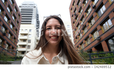 Portrait of an attractive woman with a beautiful smile and long hair against the backdrop of a residential area on a summer day. 142489512