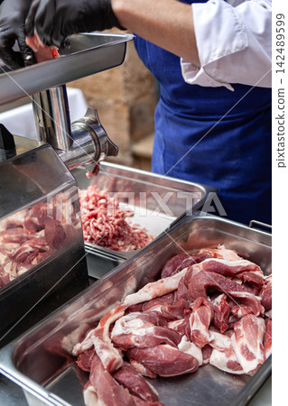 The butcher puts the pork into a meat grinder The butcher puts the pork into a meat grinder 142489599