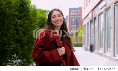 Portrait photo of happy young smiling woman in burgundy coat during city walk outdoors Portrait photo of happy young smiling woman in burgundy coat during city walk outdoors 142489677