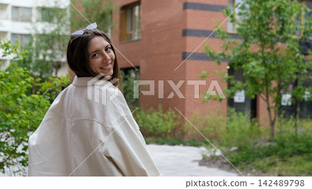 Portrait of an attractive woman with a beautiful smile and long hair against the backdrop of a residential area on a summer day. Portrait of an attractive woman with a beautiful smile and long hair against the backdrop of a residential area on a summer day. 142489798