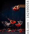 Bartender pouring red drink into cocktail glass, creating splash with pomegranate seeds 142490054