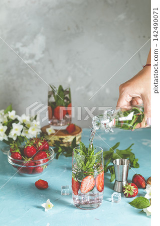 Bartender pouring water into glass with strawberries and mint Bartender pouring water into glass with strawberries and mint 142490071