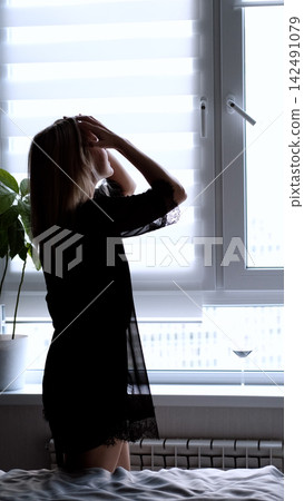 A sexy beautiful woman in a black erotic negligee stands near the window in the bedroom. A sexy beautiful woman in a black erotic negligee stands near the window in the bedroom. 142491079