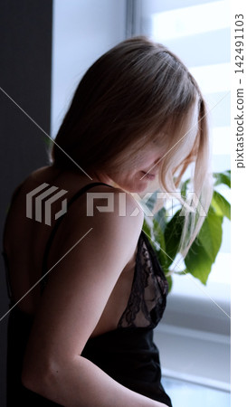 A sexy beautiful woman in a black erotic negligee stands near the window in the bedroom. A sexy beautiful woman in a black erotic negligee stands near the window in the bedroom. 142491103