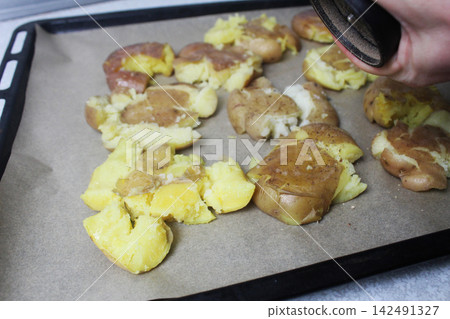 Cooking crispy roasted smashed baked potatoes. Sprinkles pepper on potatoes. Cooking crispy roasted smashed baked potatoes. Sprinkles pepper on potatoes. 142491327