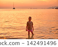 Young girl standing in shallow water with arms raised wide enjoying golden sunset at Sunset Beach, Koh Lipe, Thailand.  142491496