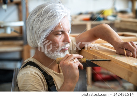 Concentrated professional craftsman restoring antique wooden furniture in carpentry workshop Concentrated professional craftsman restoring antique wooden furniture in carpentry workshop 142491514