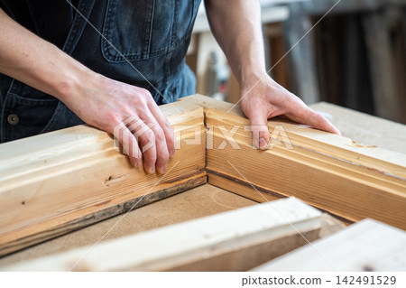 Carpenter assembling wooden parts of vintage window frame at workbench in restoration workshop. Carpenter assembling wooden parts of vintage window frame at workbench in restoration workshop. 142491529