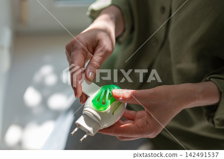 Woman inserts mosquito repellent mat into electric fumigator for indoor insect protection. Woman inserts mosquito repellent mat into electric fumigator for indoor insect protection. 142491537