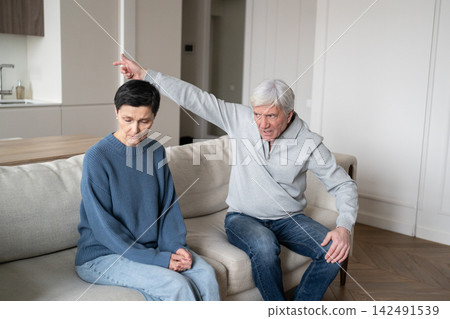 Angry hysterical elderly husband berating wife with gaslighting behavior, woman in fear on sofa Angry hysterical elderly husband berating wife with gaslighting behavior, woman in fear on sofa 142491539