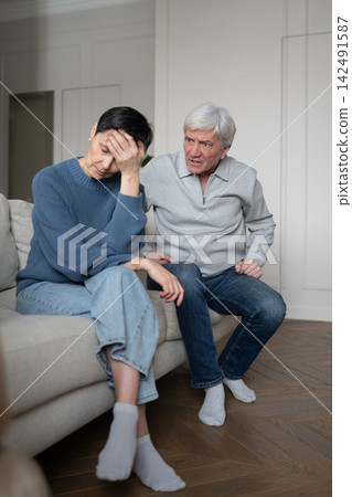 Exhausted unhappy senior woman sitting on sofa tired of angry conversation with elderly husband. Exhausted unhappy senior woman sitting on sofa tired of angry conversation with elderly husband. 142491587