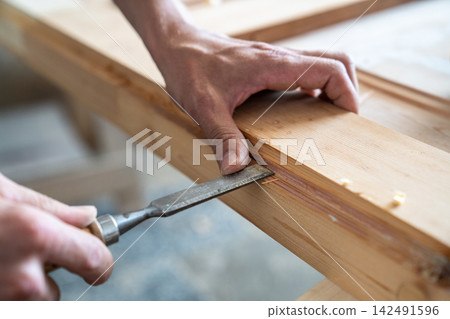 Master deeply carving surface of antique wooden door at workbench in carpentry with chisel tool 142491596