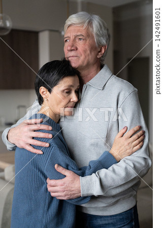 Tired mature wife with closed eyes being tightly embraced by husband, seeking emotional support Tired mature wife with closed eyes being tightly embraced by husband, seeking emotional support 142491601