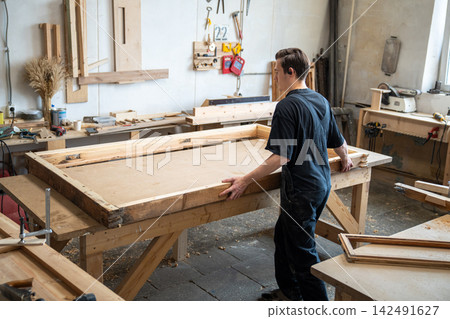 Carpenter preparing wooden window frame for renovation at workbench in carpentry workshop. 142491627