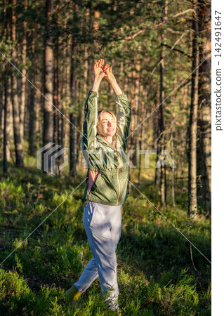 Woman walking through autumn pine forest, breathes in the forest air and raising both hands together Woman walking through autumn pine forest, breathes in the forest air and raising both hands together 142491647