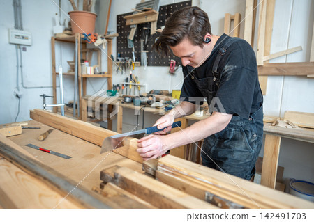 Focused restorer master preparing part of wooden frame for restoration at worktable in workshop. Focused restorer master preparing part of wooden frame for restoration at worktable in workshop. 142491703