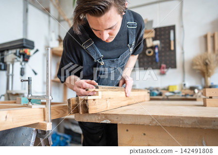 Talented man carpenter renovating vintage wooden frame, precisely picks wooden patch for replacement Talented man carpenter renovating vintage wooden frame, precisely picks wooden patch for replacement 142491808