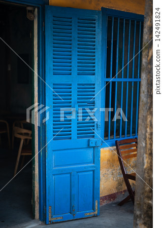 Vintage blue colored wooden doors and table with chairs setting in traditional cafe in Hoi An. Vintage blue colored wooden doors and table with chairs setting in traditional cafe in Hoi An. 142491824