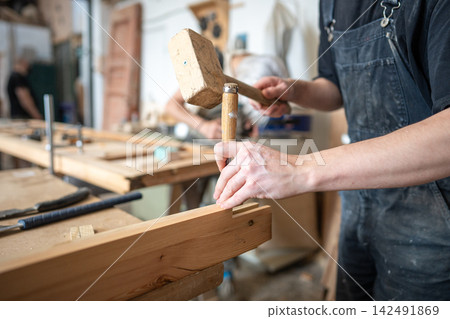 Hardworking carpenter in restoration workshop renovating wooden frame with mallet and chisel tools. 142491869