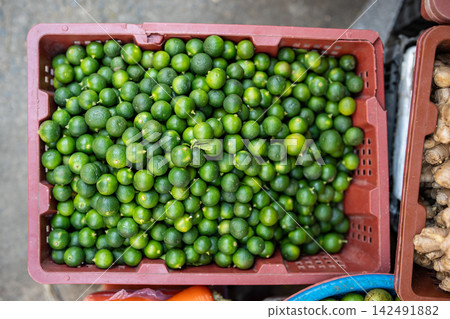 Plastic container filled with fresh ripe green lime fruits selling by vendor at outdoor marketplace. Plastic container filled with fresh ripe green lime fruits selling by vendor at outdoor marketplace. 142491882