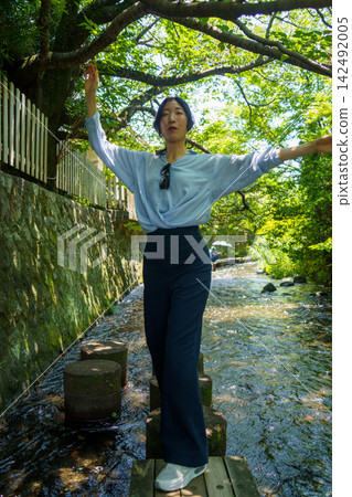 一位三十多歲的日本女子站在清澈溪流中的踏腳石上，雙臂伸展。 142492005