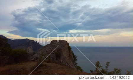 scenic rocky cliff with natural arch and panoramic view of calm sea under cloudy sunset sky scenic rocky cliff with natural arch and panoramic view of calm sea under cloudy sunset sky 142492032