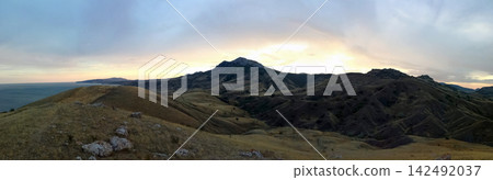 majestic mountain massif over hilly valley and sea under bright glowing setting sun majestic mountain massif over hilly valley and sea under bright glowing setting sun 142492037