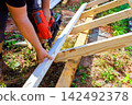 Worker is fastening wooden beams on construction site using air pneumatic nail gun 142492378
