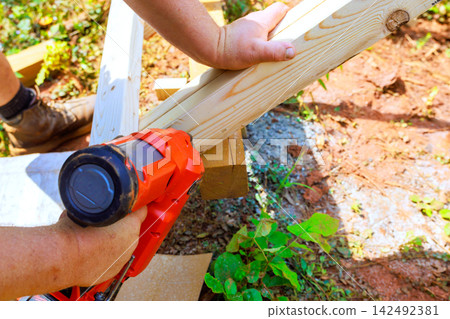 Construction worker is at work fastening wooden boards together using power nail gun tool. 142492381