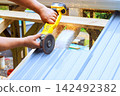Worker uses power tool to cut metal sheet on construction site in sparks fly from cutting process. 142492382