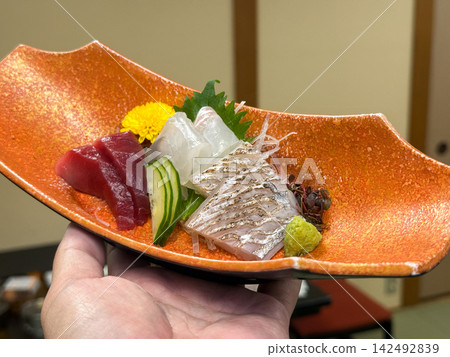 三種刺身：鮪魚、鯛魚和炙烤帶魚，盛放在橘色的日本餐具中。 142492839