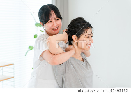 一位女士正在接受按摩師的頸部和肩部伸展治療。 一位女士正在接受按摩師的頸部和肩部伸展治療。 142493182